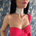 May include: A pearl choker necklace with a gold clasp and a central diamond. The multi-strand necklace is worn around the neck. The model is wearing a red dress.